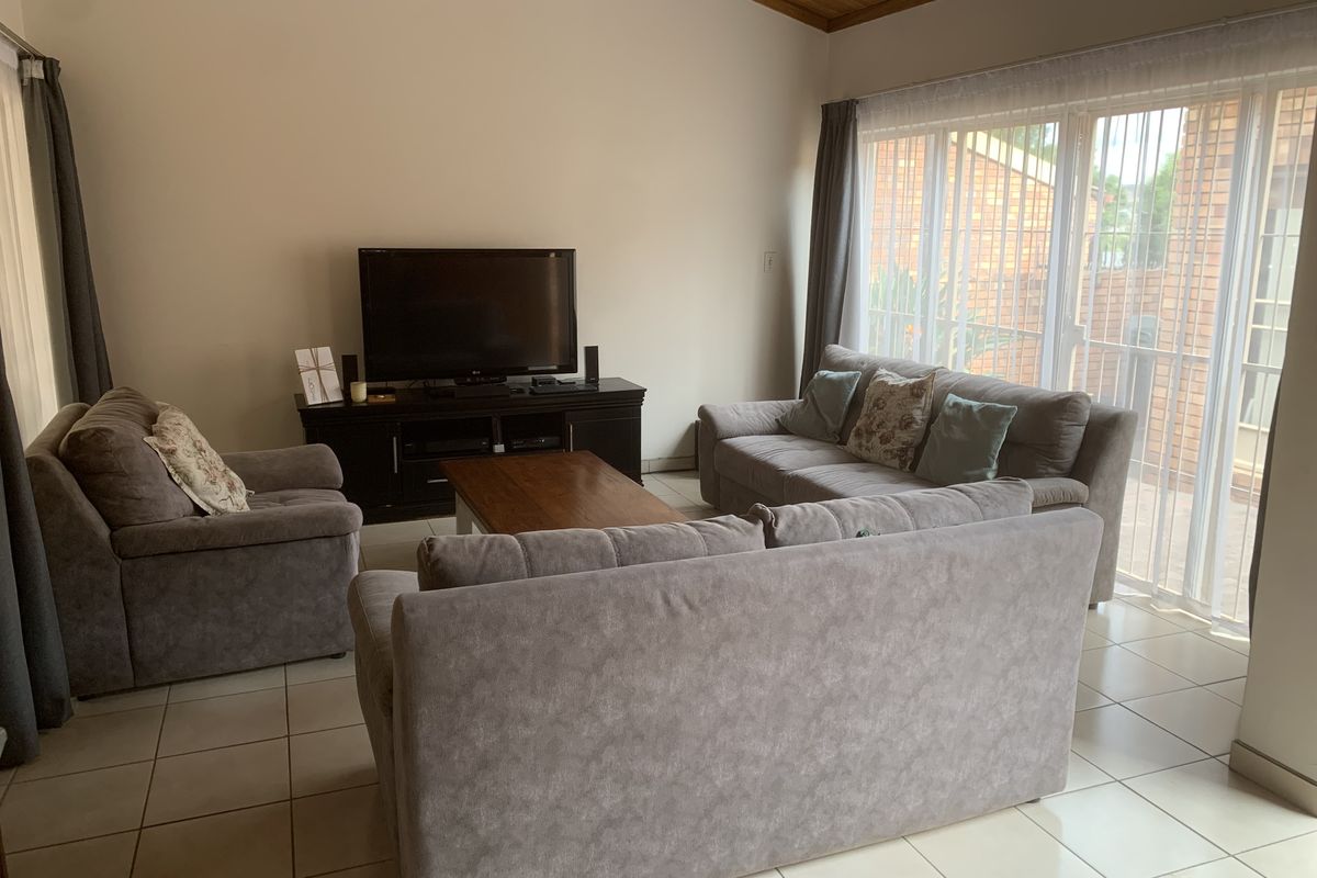 A comfortable living room featuring tiled flooring, a distinctive timber-clad vaulted ceiling, and large sliding glass doors that provide access to the patio.
