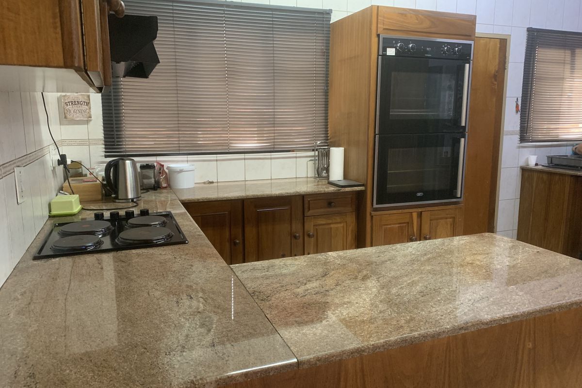 A functional kitchen featuring granite countertops, wooden cabinetry, a built-in double oven, and an electric hob with an extractor fan.