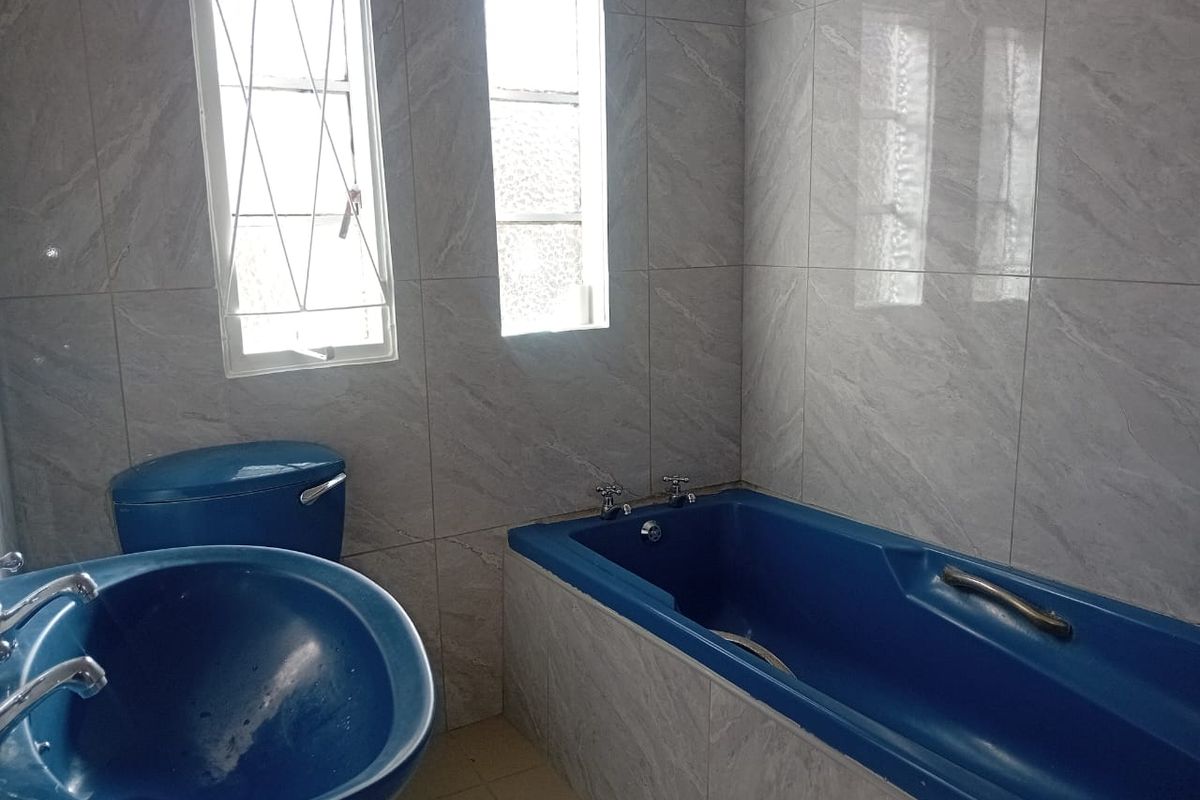 A bathroom featuring grey wall tiles, a blue bathtub, and a matching blue pedestal basin with chrome taps.