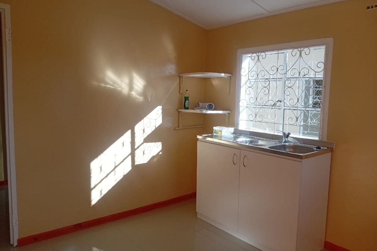 A basic kitchen area featuring a single sink unit with white cabinetry, tiled flooring, and security bars on the window.