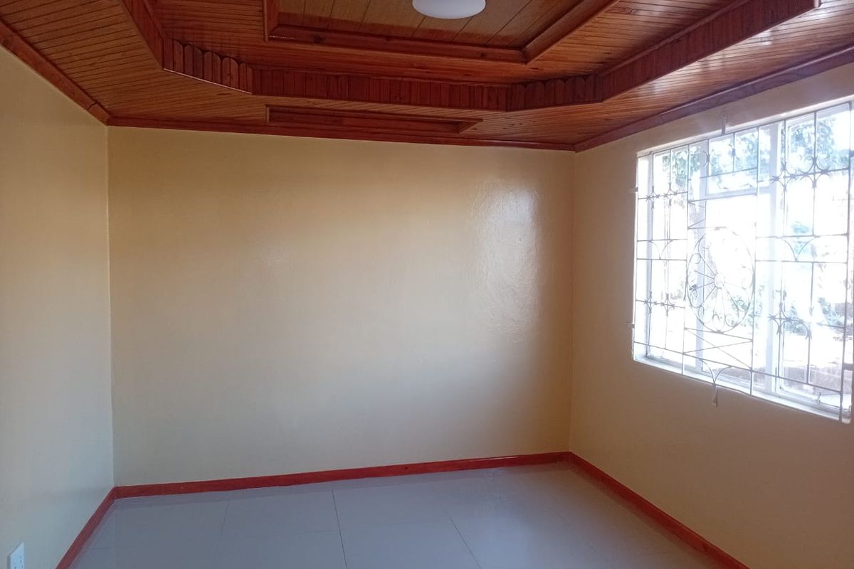 An empty bedroom featuring a distinctive timber-paneled tray ceiling, tiled flooring, and a window fitted with decorative security burglar bars.