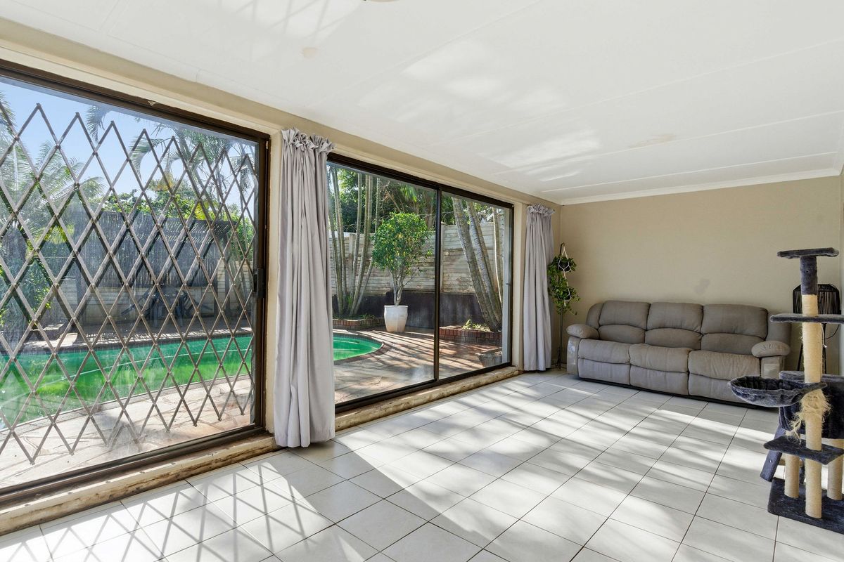 Spacious living area featuring large sliding glass doors with security gates, providing direct access to the pool area and garden.