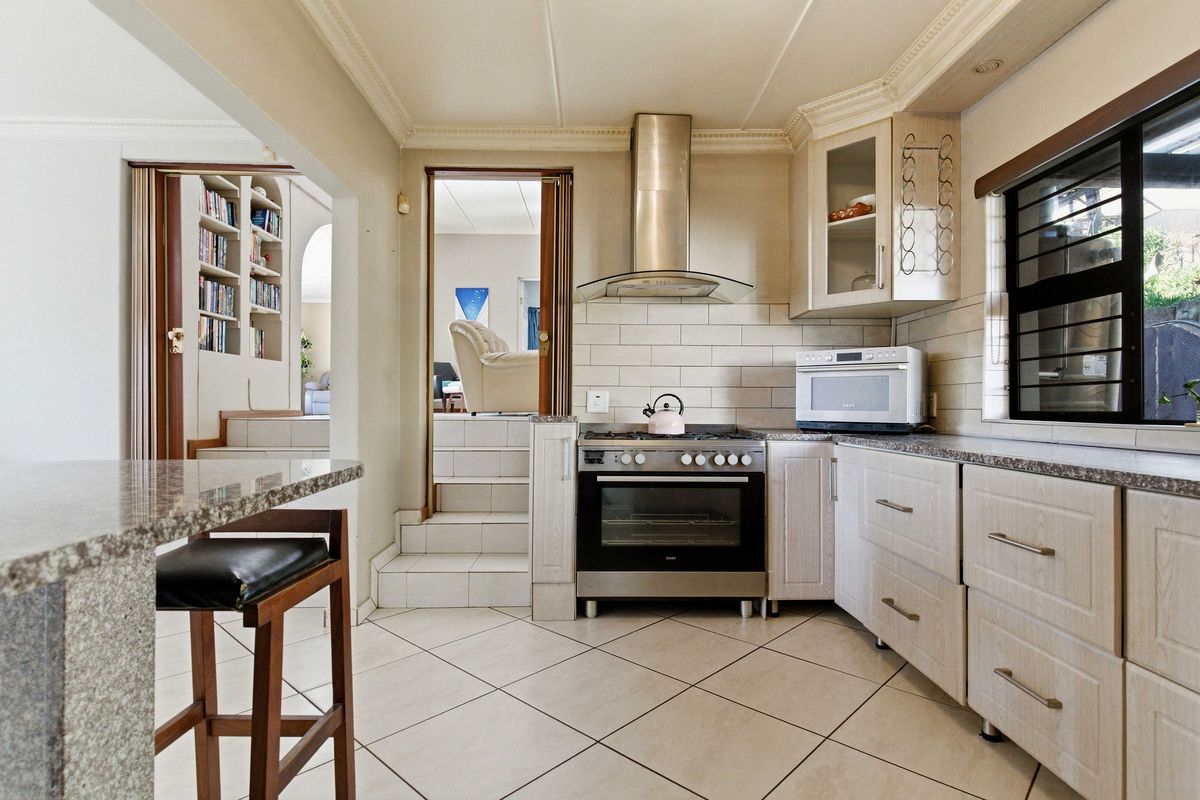 A functional kitchen featuring granite countertops, stainless steel appliances, tiled flooring, and built-in cabinetry with a convenient breakfast bar area.