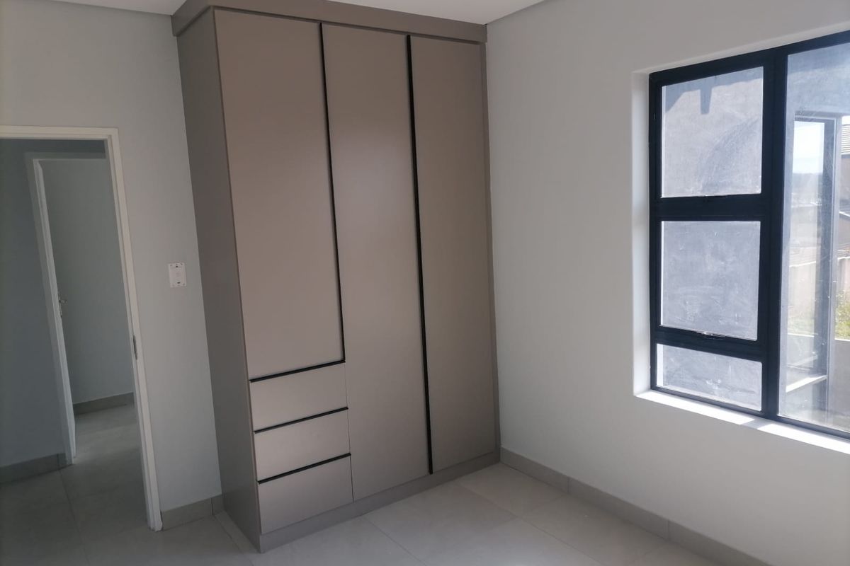 A bright bedroom featuring modern built-in cupboards with a sleek finish, tiled flooring, and a large window allowing for natural light.