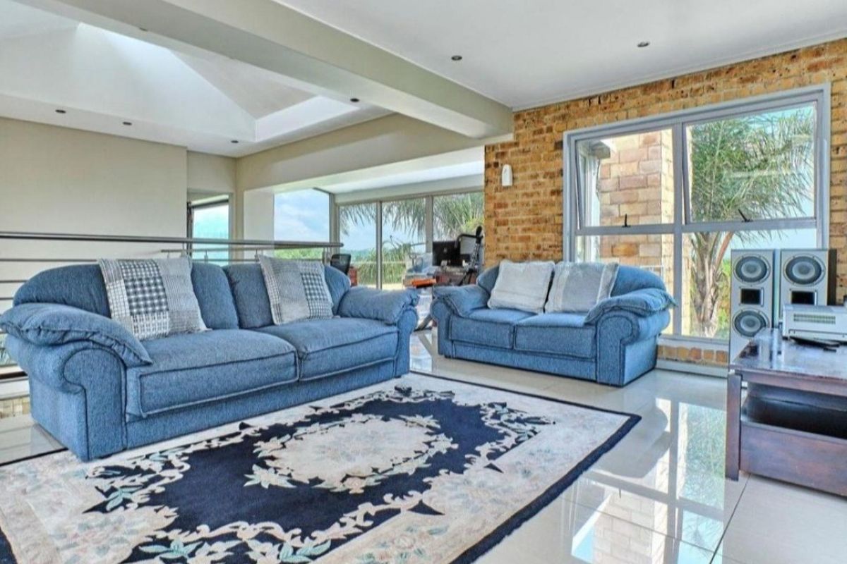 Spacious living area featuring an exposed brick feature wall, large windows providing natural light, vaulted ceilings, and polished tiled flooring.