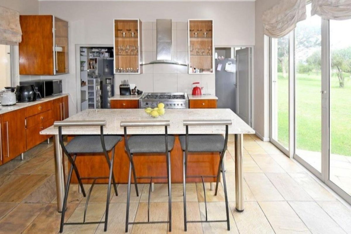 Spacious kitchen featuring a central stone-topped island, wooden cabinetry, gas stove with extractor, and direct access to the garden through large sliding glass doors.