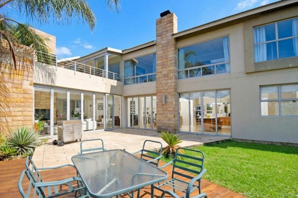 Spacious rear exterior featuring a stone chimney, extensive folding glass doors, a stone patio, and a timber deck overlooking the garden.