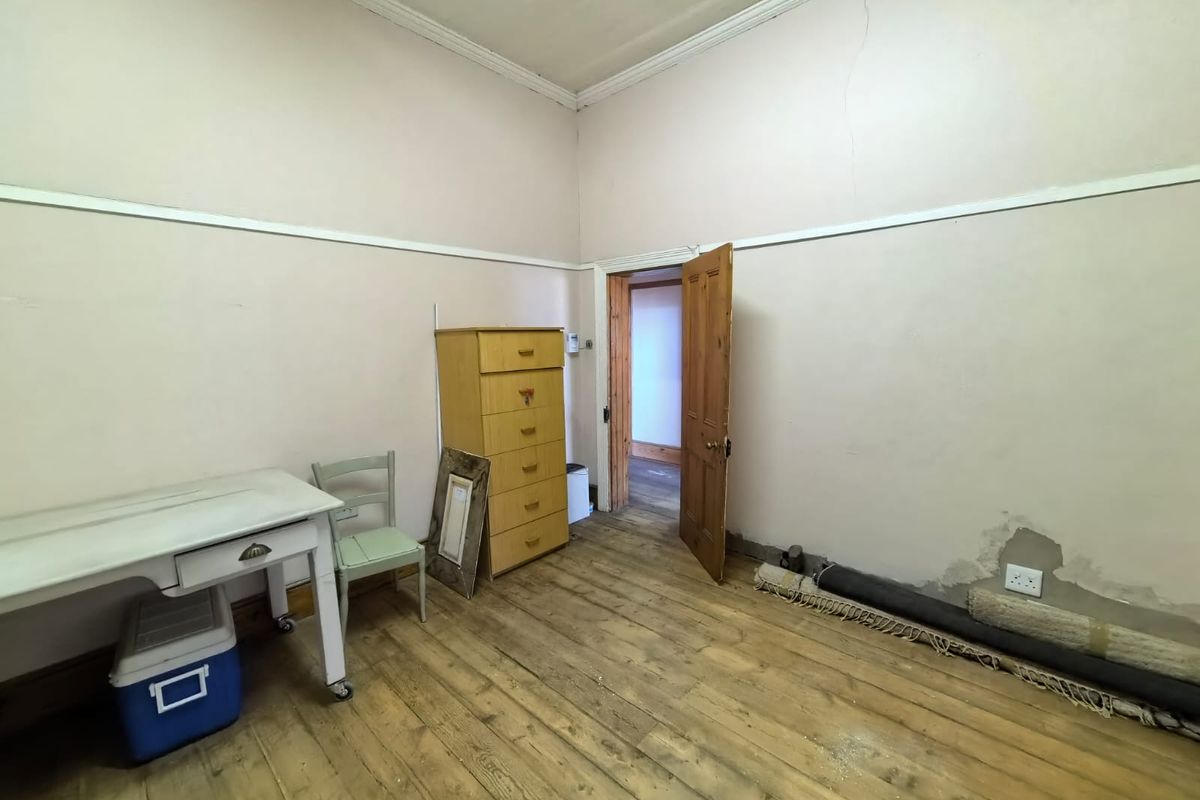 A bedroom featuring original timber flooring, picture rails, and cornice detailing, currently requiring cosmetic repairs to the wall plaster and flooring.