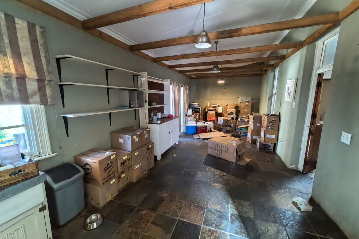 Spacious kitchen area featuring rustic exposed timber ceiling beams, slate tile flooring, and built-in storage shelving, offering significant potential for modernization.
