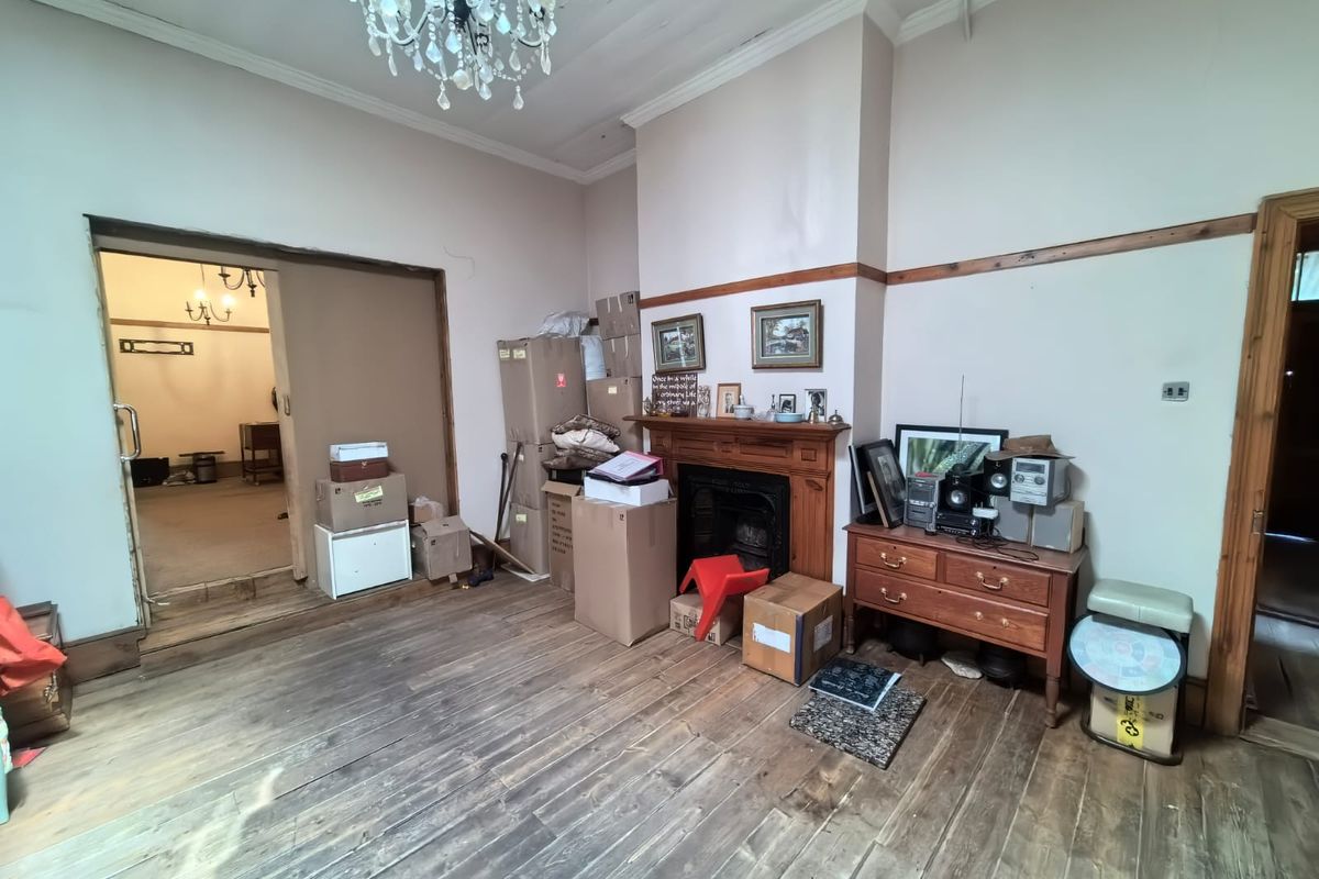 Living room featuring original timber flooring, a traditional fireplace with a timber mantelpiece, and classic ceiling detailing, offering significant potential for restoration.