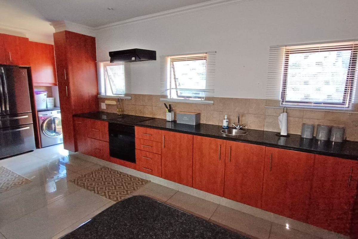 A functional kitchen featuring warm-toned cabinetry, granite countertops, built-in oven, extractor fan, and tiled splashbacks with ample natural light.