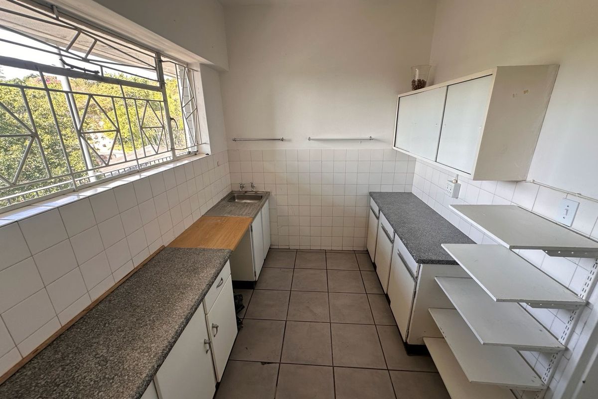 A functional kitchen space featuring tiled walls, stone-look countertops, built-in cabinetry, and a stainless steel sink with large windows providing natural light.