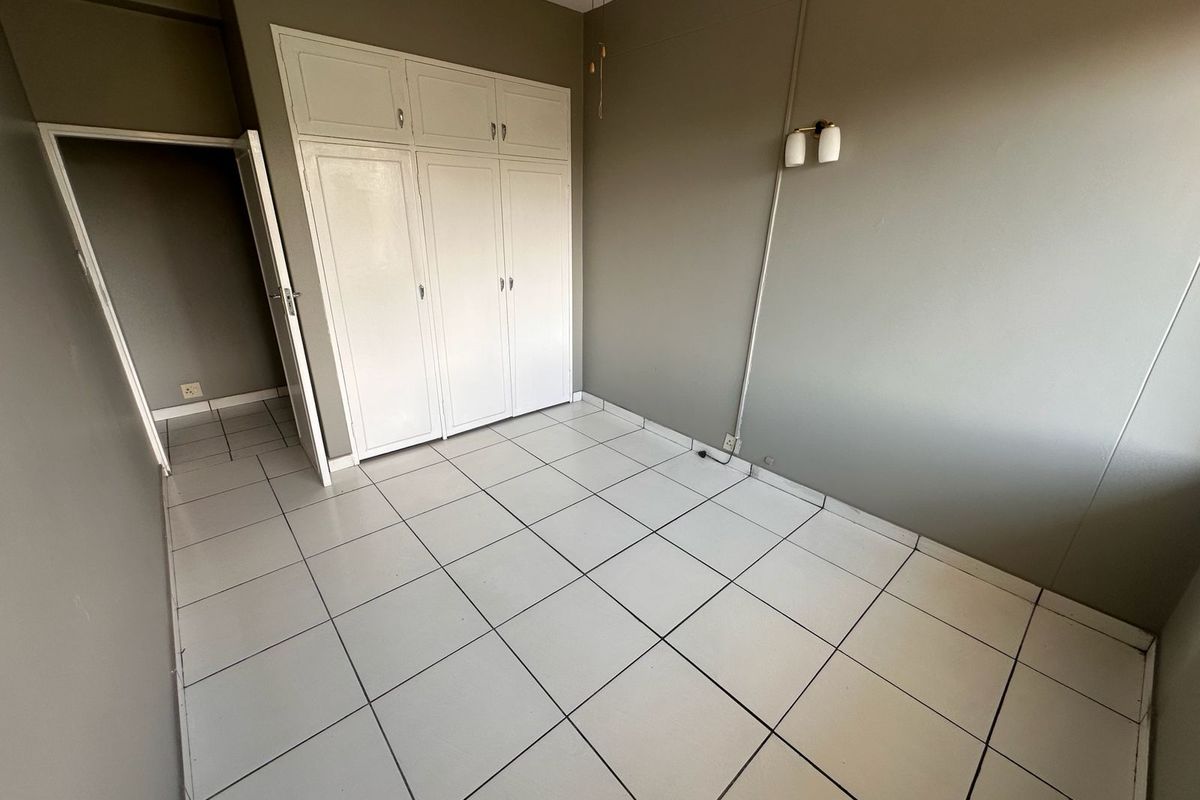 An empty bedroom featuring white tiled flooring, built-in storage cupboards, and wall-mounted lighting fixtures.