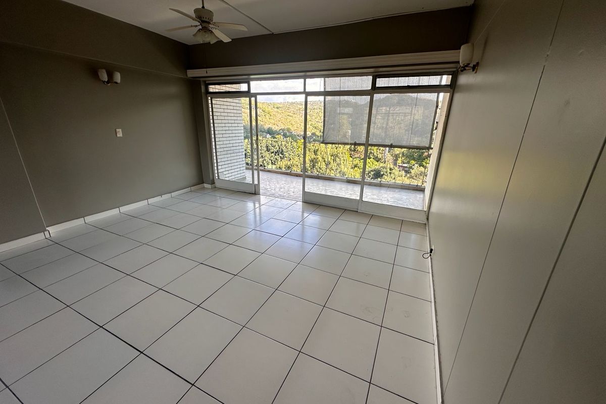 Spacious living area featuring white tiled flooring, a ceiling fan, and large sliding glass doors opening onto a balcony with scenic views.