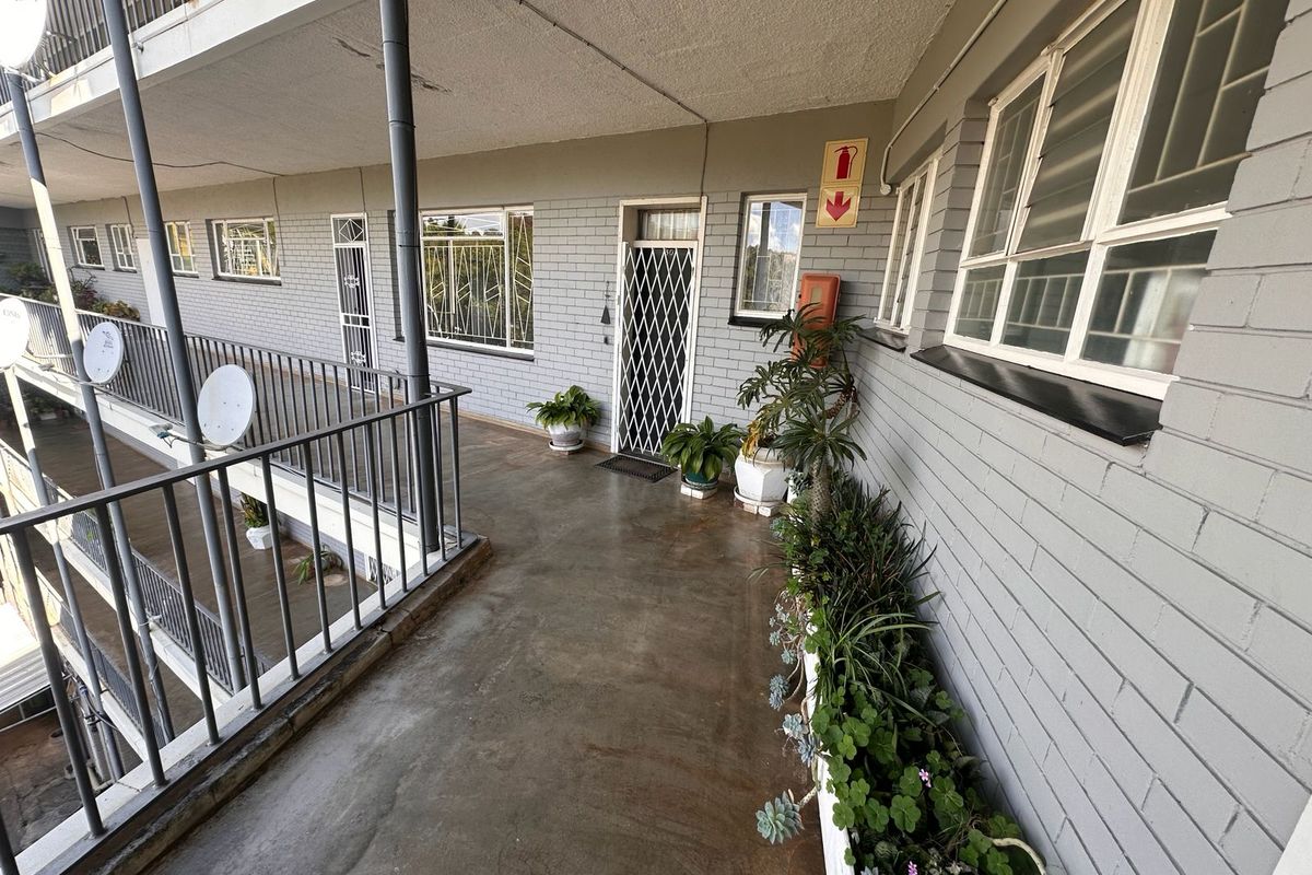 An exterior apartment walkway featuring painted brick walls, metal security gates, and a metal balustrade overlooking the building complex.