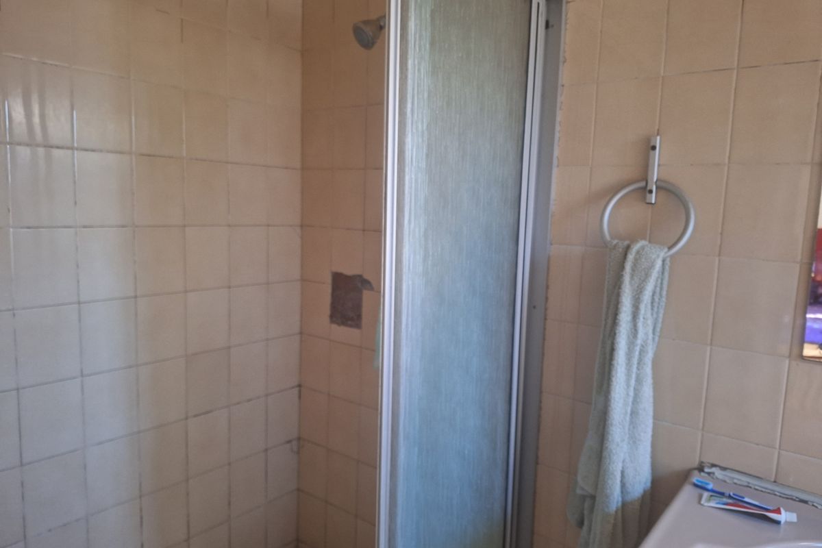 A dated bathroom featuring a shower enclosure with tiled walls and a vanity basin, showing signs of wear and requiring cosmetic updates.