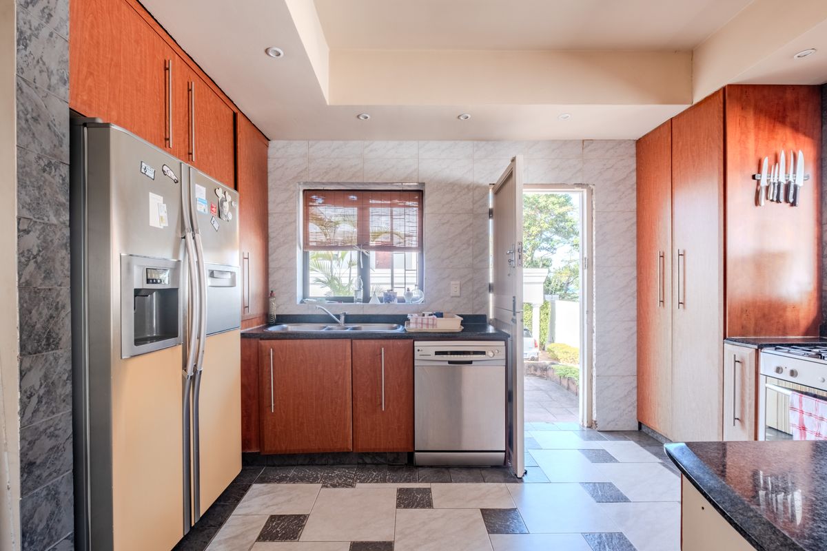 A functional kitchen featuring wood-toned cabinetry, stone countertops, integrated appliances, and direct access to the exterior through a side door.