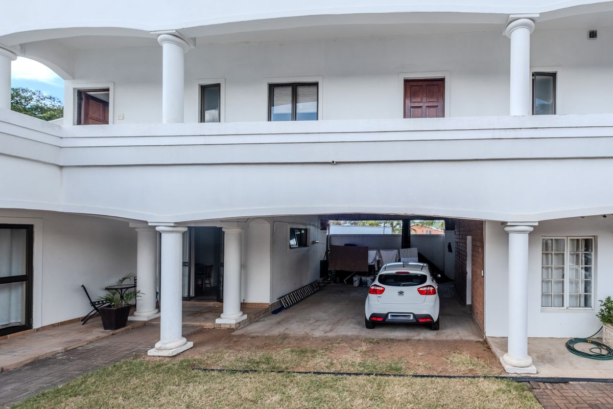 Rear view of a multi-story house featuring a covered patio area, balcony, and paved driveway space.