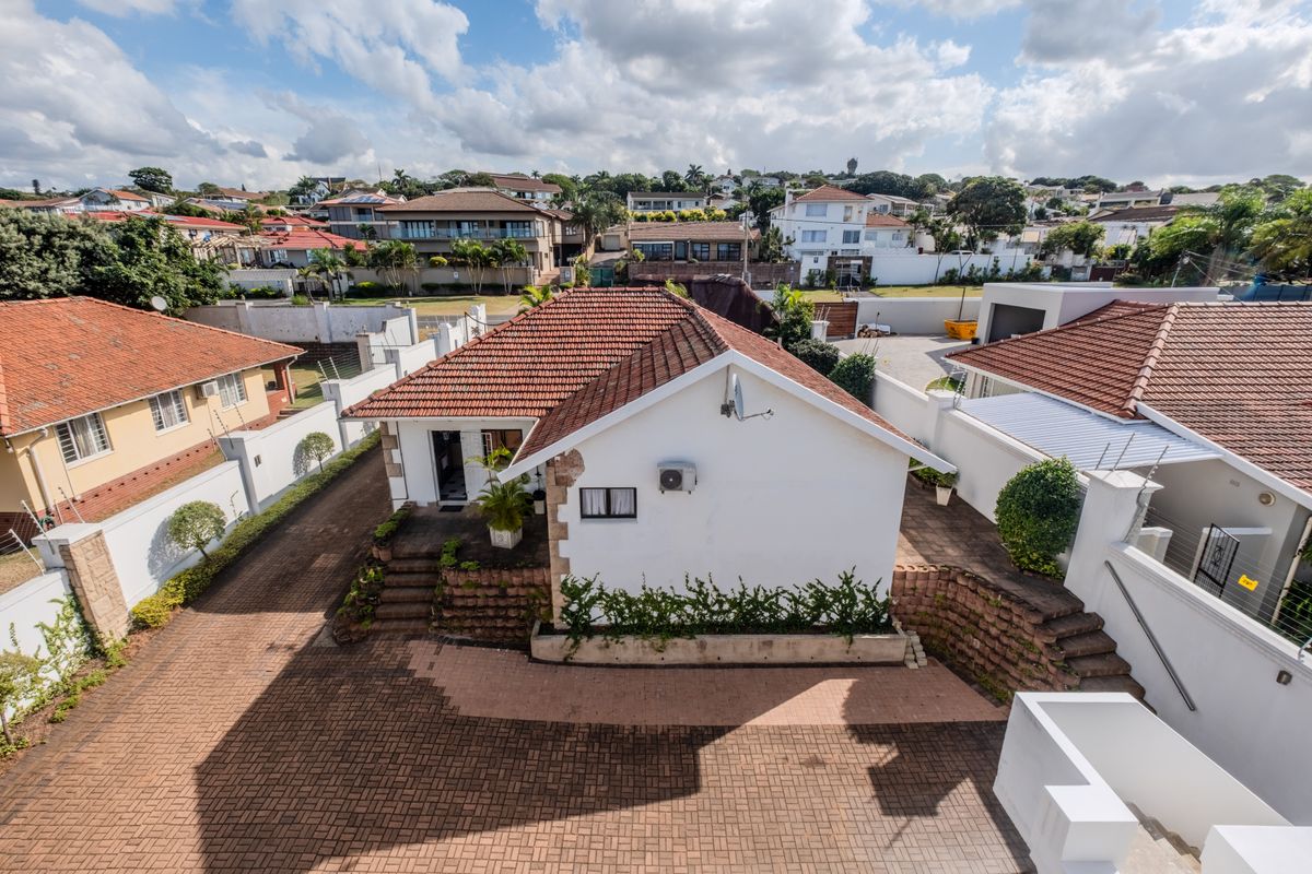 Aerial view of the property showing the main building, tiled roof, paved driveway, and surrounding boundary walls in a residential neighborhood.