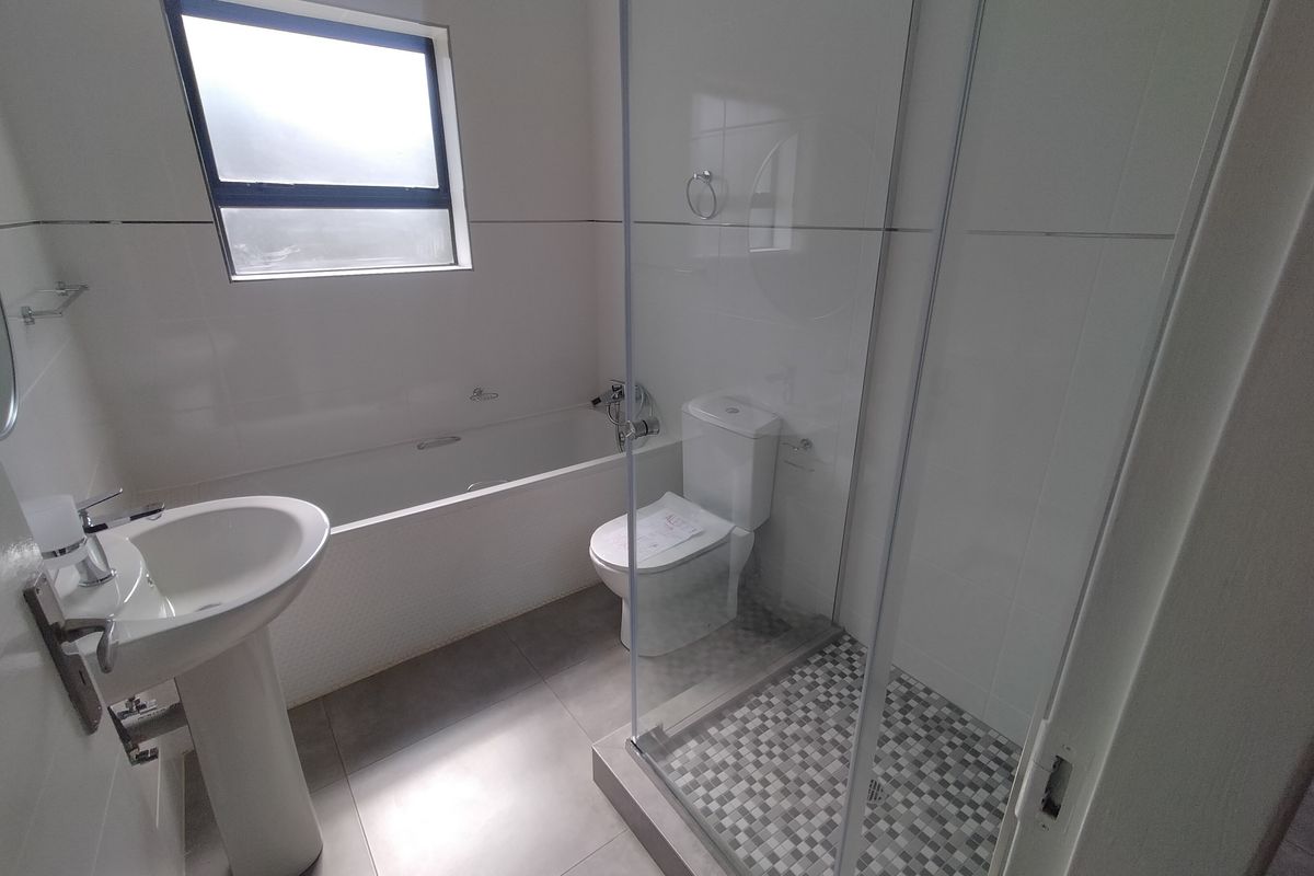 A clean, modern bathroom featuring a pedestal basin, built-in bathtub, and a separate glass-enclosed shower with mosaic floor tiling.