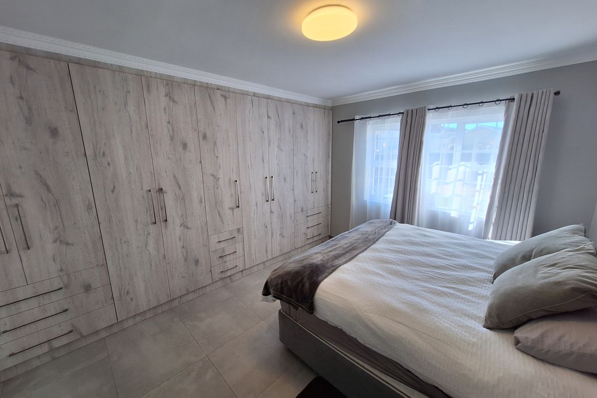 A well-maintained bedroom featuring extensive built-in cabinetry with wood-grain finish, neutral tiled flooring, and classic ceiling cornice detailing.
