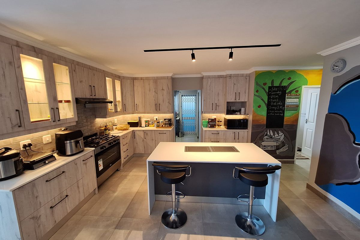 Modern kitchen featuring light wood-grain cabinetry, a central island with seating, gas hob, built-in oven, and contemporary track lighting.