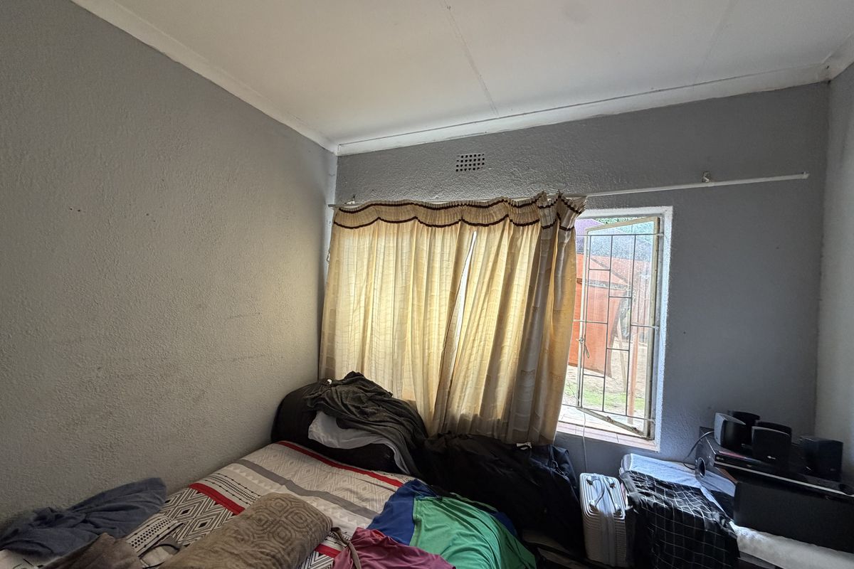 A bedroom featuring a window with security bars and basic wall finishes, offering a functional space ready for cosmetic updates.