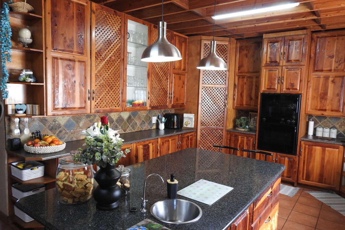 A rustic kitchen featuring extensive solid wood cabinetry, a central island with a granite countertop, integrated sink, and exposed timber ceiling beams.