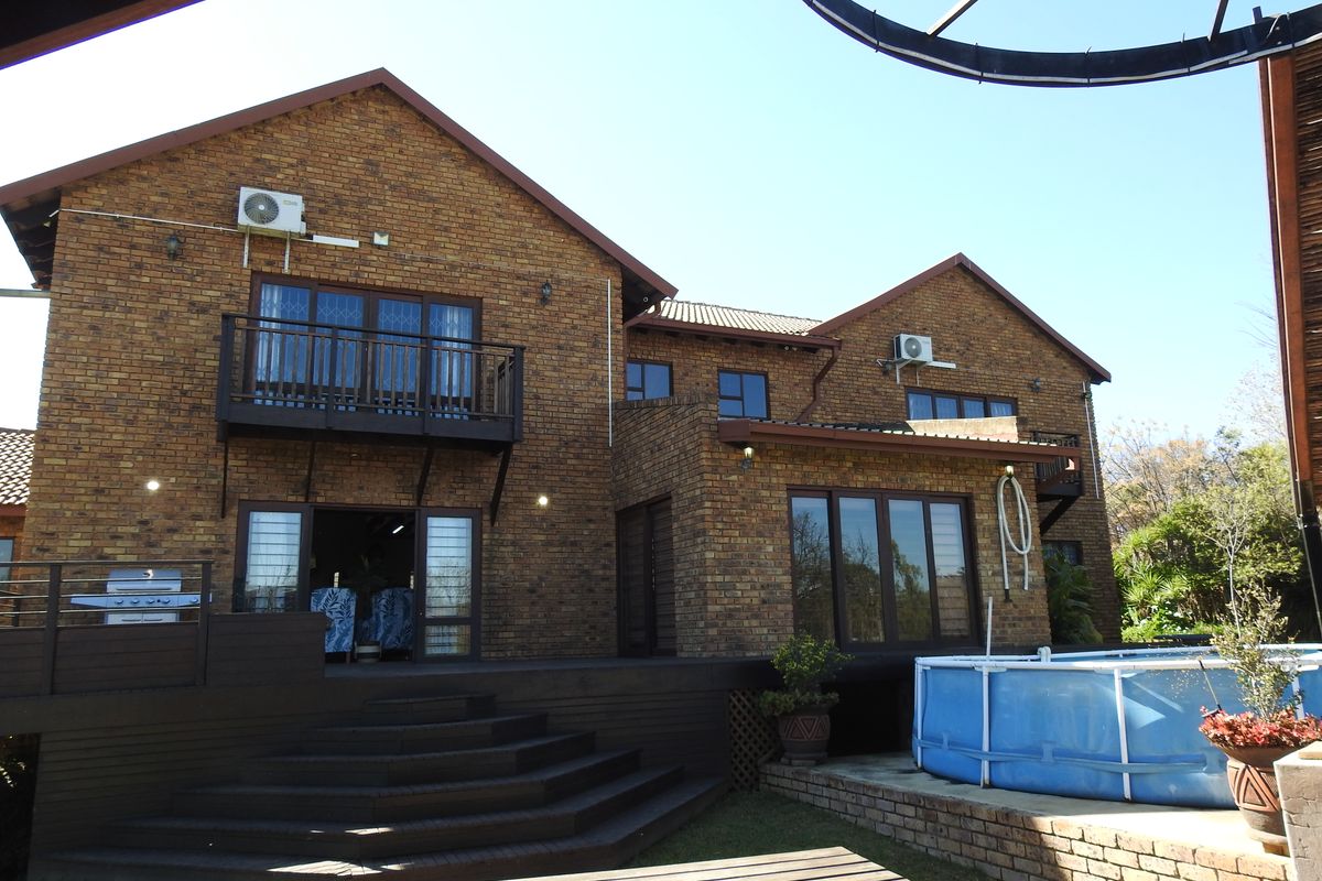 Rear view of a double-story face-brick home featuring a wooden deck, balcony, and an outdoor pool area.
