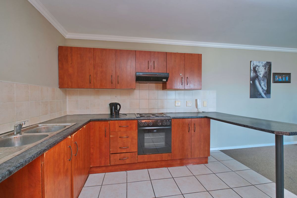A functional kitchen featuring wood-look laminate cabinetry, dark countertops, a built-in oven with hob, and a breakfast bar extension.