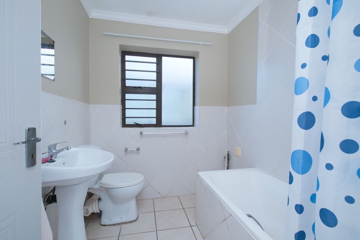 A functional bathroom featuring a pedestal basin, toilet, and bathtub with tiled finishes and a window with security bars.