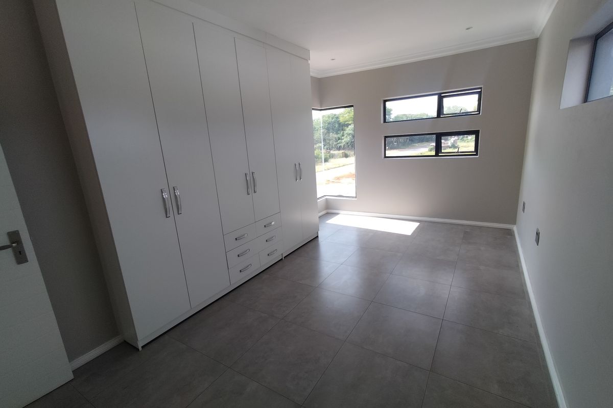 A bright, modern bedroom featuring neutral walls, large format floor tiles, and extensive built-in cupboard storage with contemporary finishes.