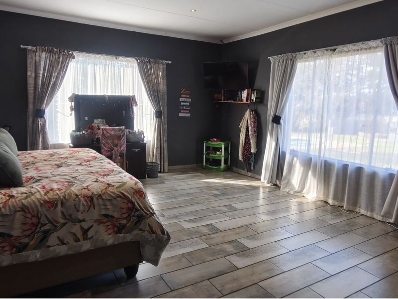 Spacious bedroom featuring dark painted walls, large windows with curtains, and modern wood-look tiled flooring.