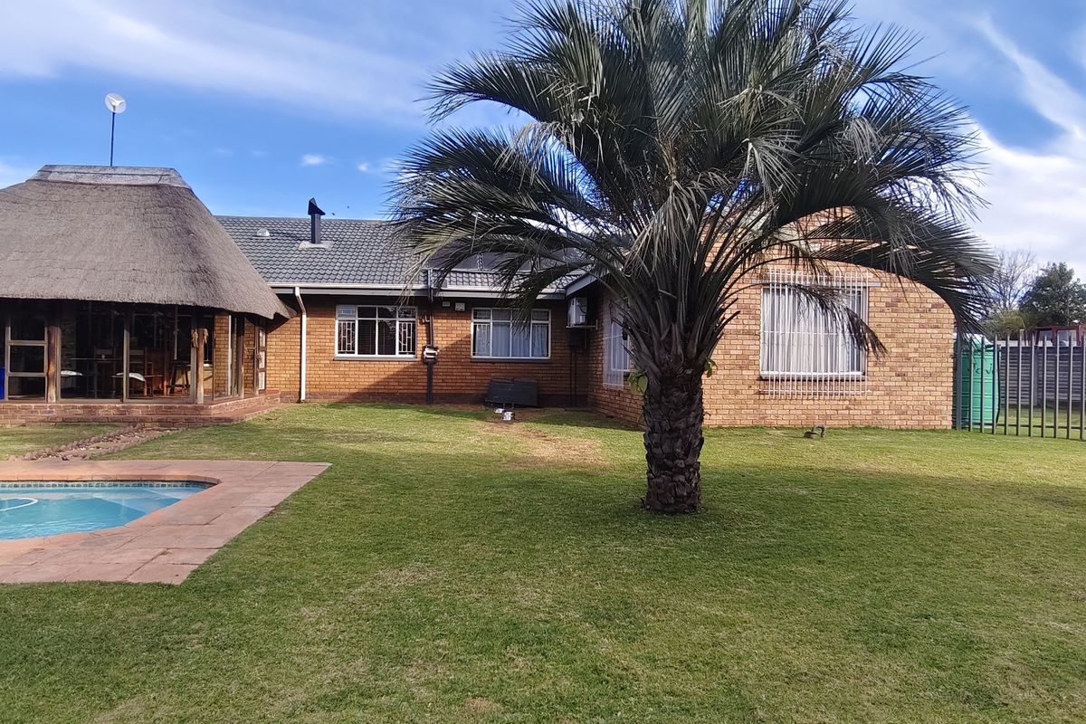 Rear view of the property featuring a brick facade, a thatched roof section, a swimming pool, and a spacious garden area.