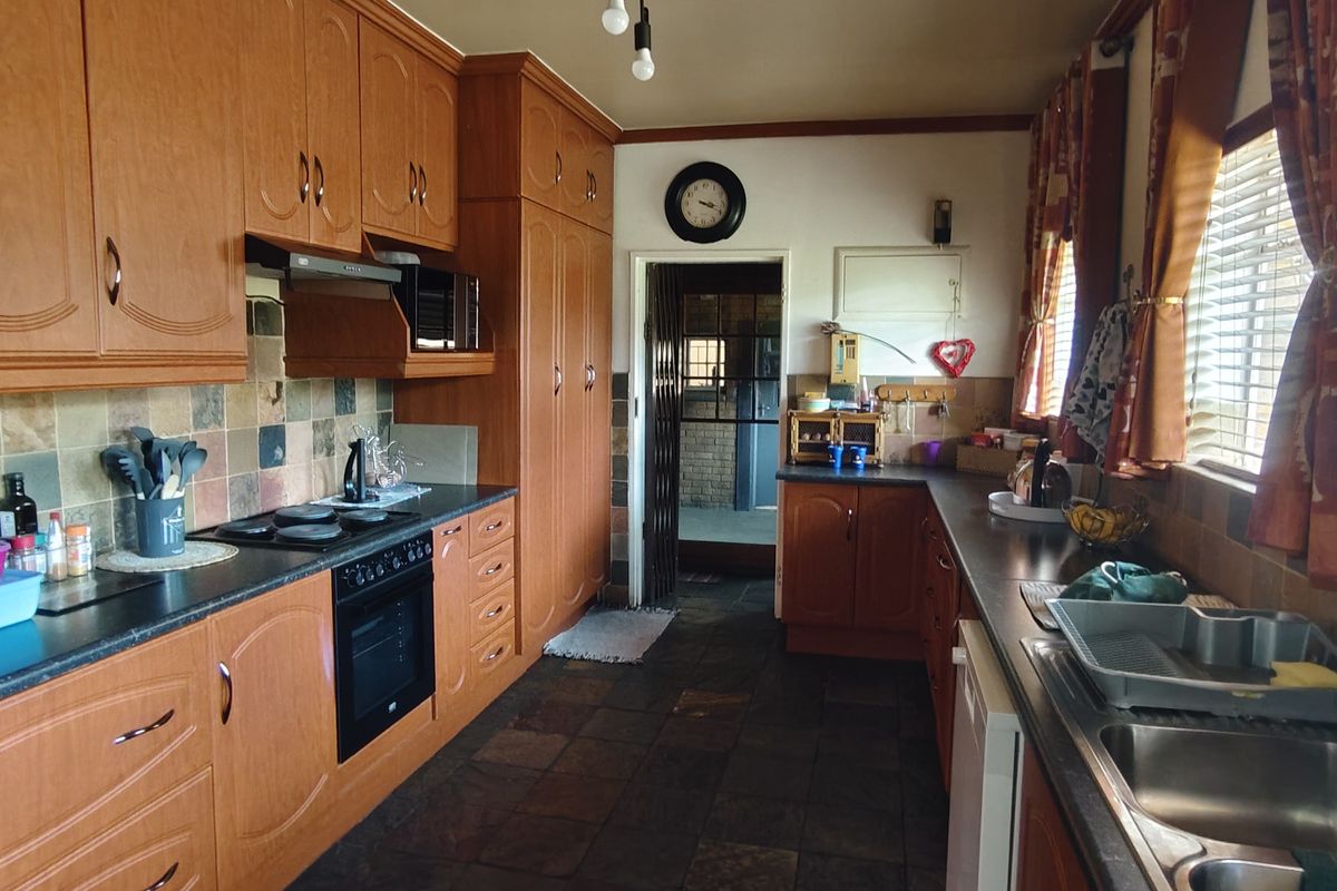 A functional kitchen featuring wood-finish cabinetry, slate tile flooring, integrated oven and hob, and a double stainless steel sink with tiled backsplash.