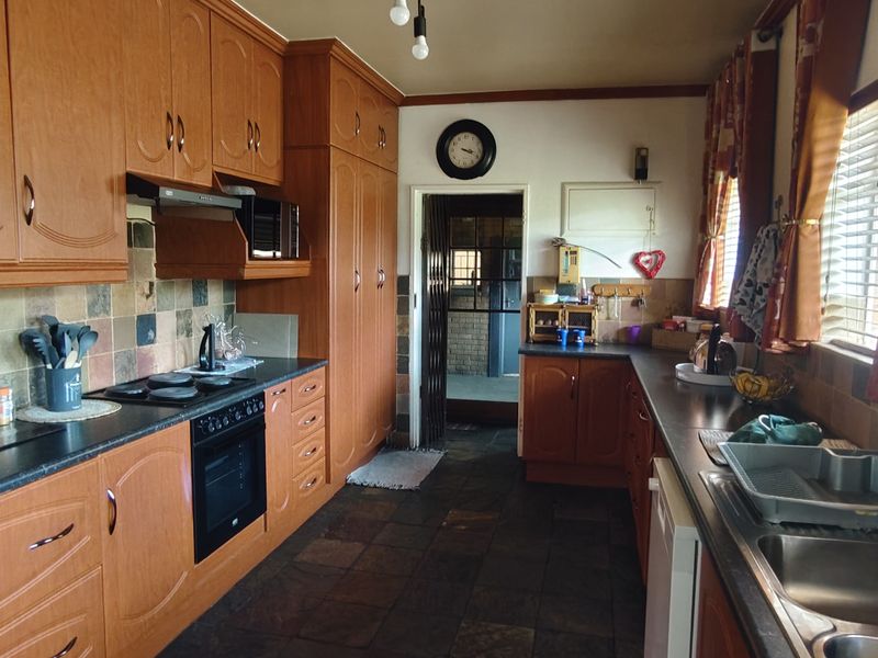 A functional kitchen featuring wood-finish cabinetry, slate tile flooring, integrated oven and hob, and a double stainless steel sink with tiled backsplash.