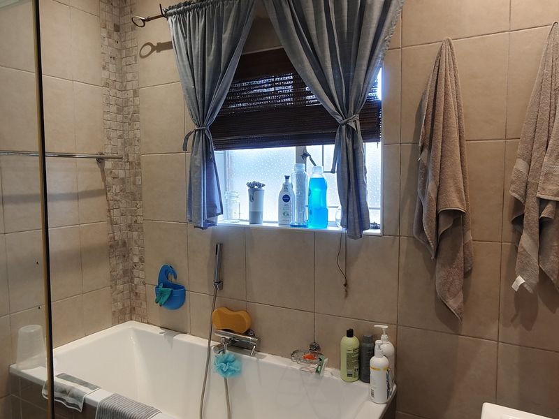 A functional bathroom featuring a built-in bathtub, a separate shower enclosure, and neutral wall tiling with decorative mosaic accents.