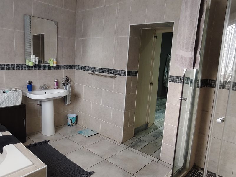 A functional bathroom featuring a pedestal basin, built-in bathtub, and a separate glass-enclosed shower with neutral ceramic tiling and a decorative mosaic border.