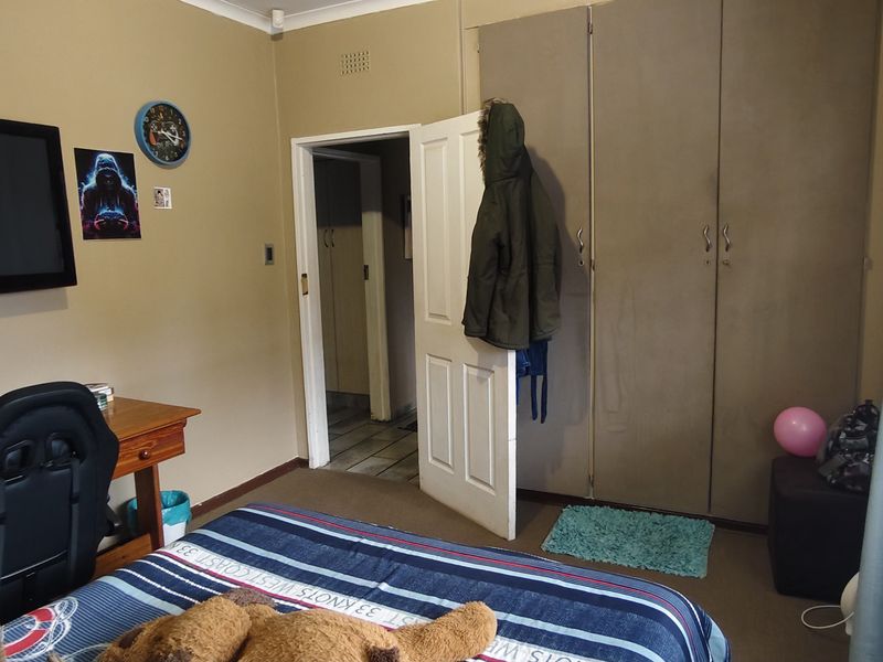 A functional bedroom featuring built-in cupboards, neutral wall finishes, and venetian blinds, providing a practical living space with standard residential fixtures.