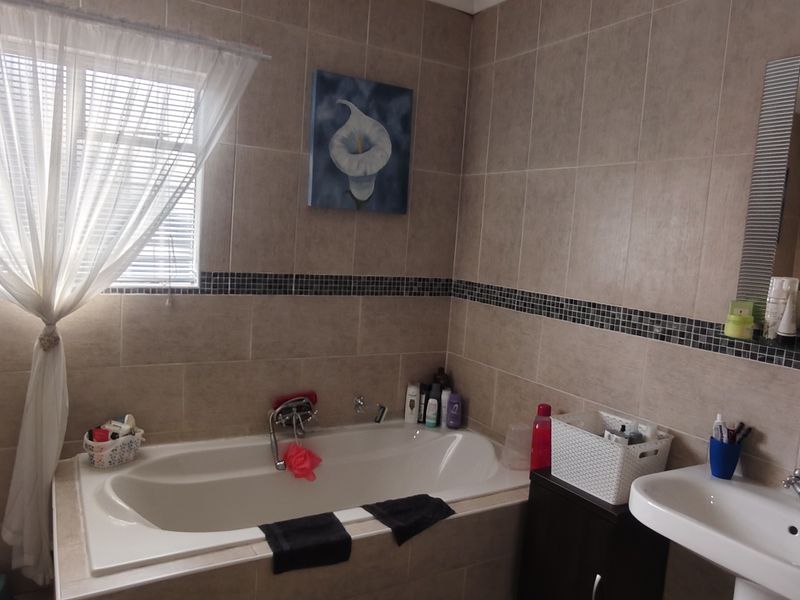 A functional bathroom featuring a built-in bathtub, pedestal washbasin, and neutral wall tiling with a decorative mosaic accent border.
