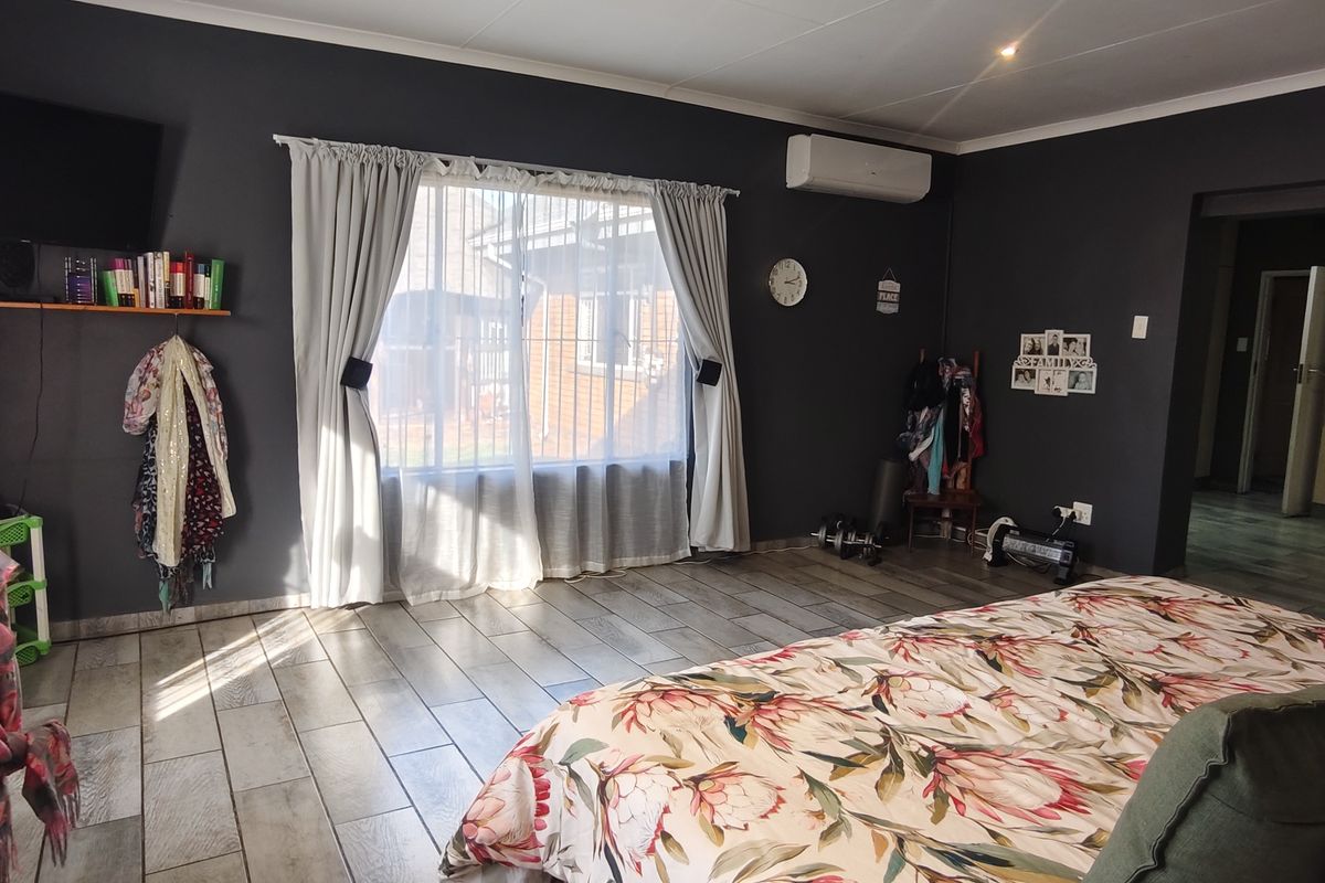 Spacious bedroom featuring tiled flooring, a wall-mounted air conditioning unit, and built-in storage cupboards.