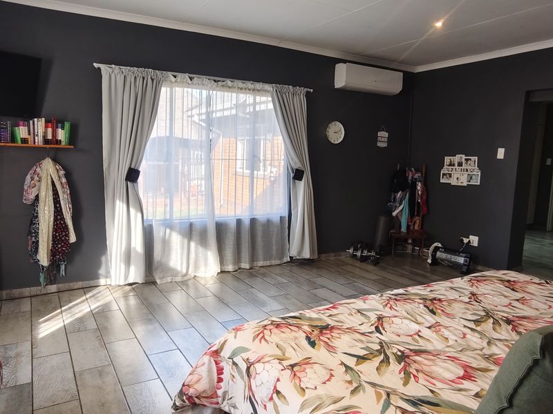 Spacious bedroom featuring tiled flooring, a wall-mounted air conditioning unit, and built-in storage cupboards.