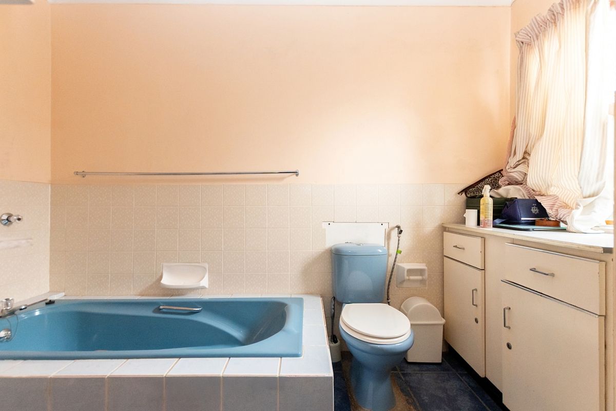 A dated bathroom featuring a blue bathtub and toilet suite with built-in vanity cabinetry and tiled splashbacks.