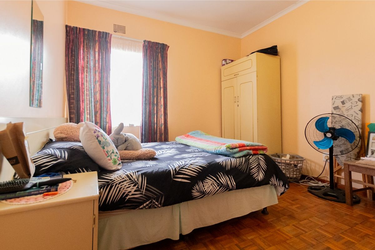 A bedroom featuring classic parquet flooring, a built-in wardrobe, and natural light from the window.
