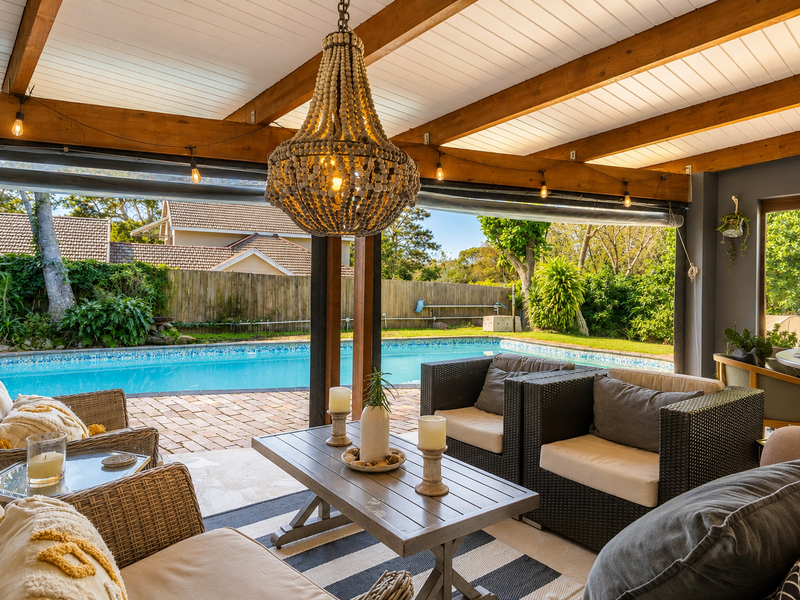 Covered outdoor patio featuring exposed timber beams and a tongue and groove ceiling, overlooking a private swimming pool and landscaped garden area.