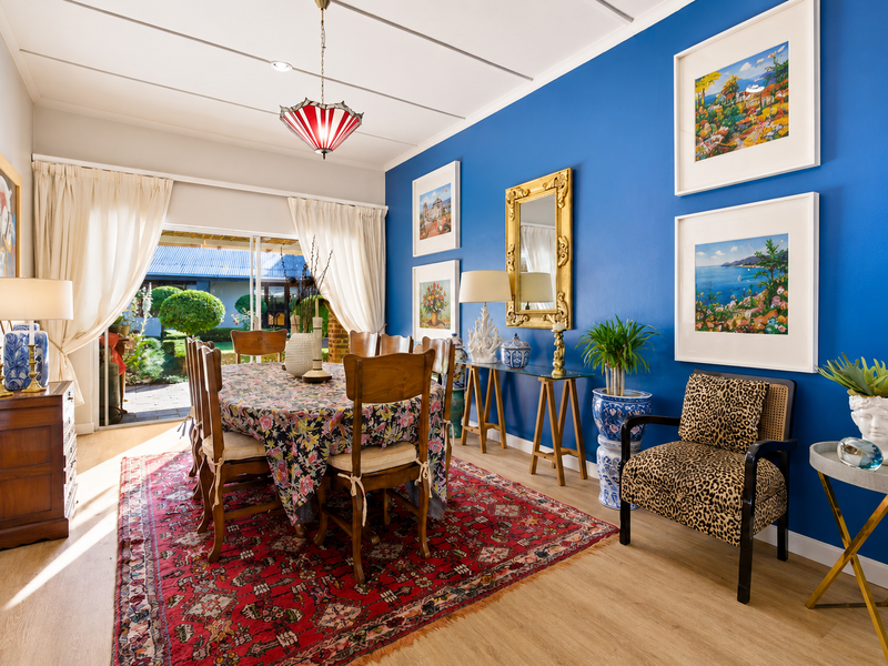 A bright dining room featuring laminate flooring, a bold blue accent wall, and sliding glass doors providing direct access to the outdoor patio area.