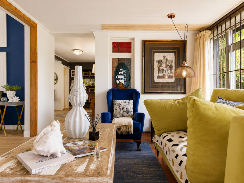 A cozy living room featuring unique stained glass accents, timber ceiling detailing, and large windows with security bars, creating a warm and character-filled space.