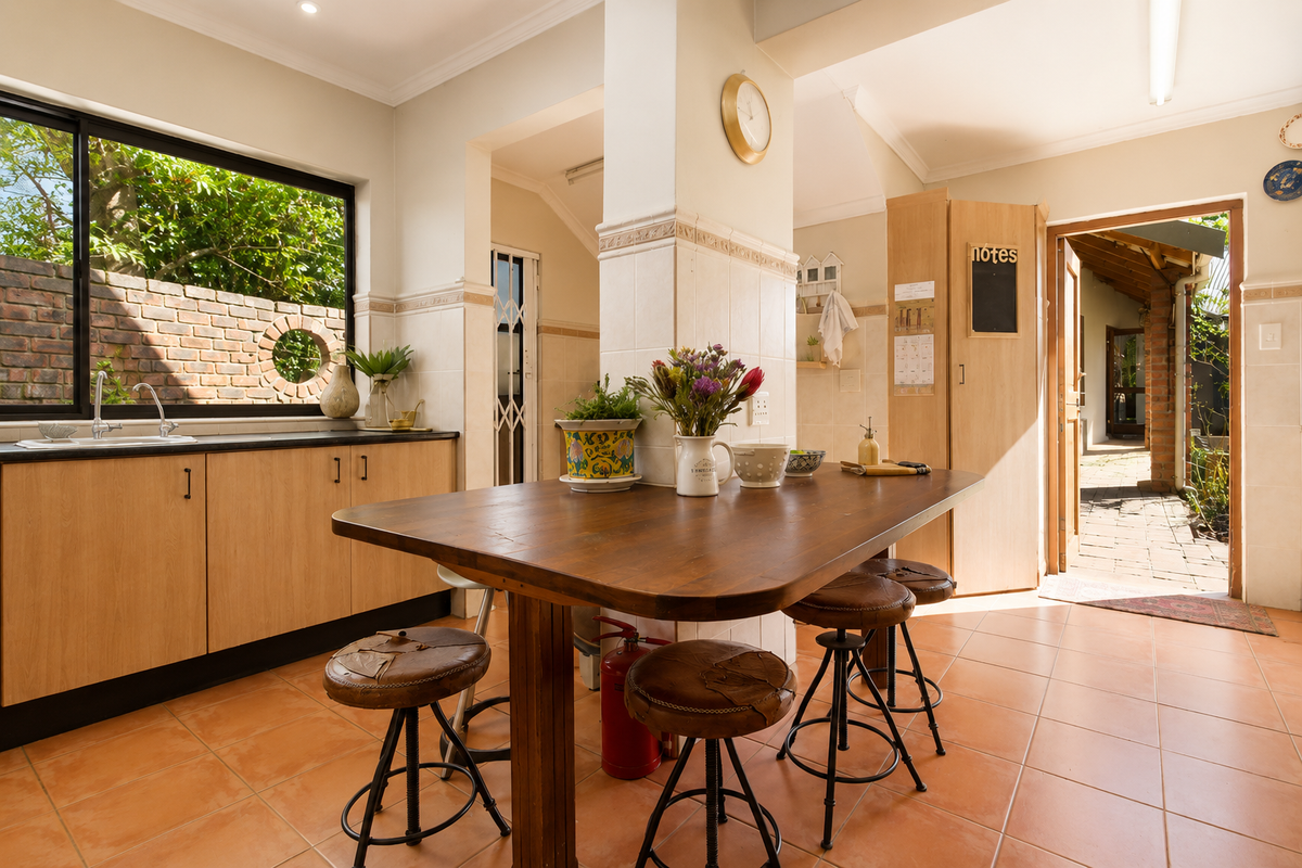 A functional kitchen featuring light wood cabinetry, tiled flooring, and a central dining area with direct access to an outdoor patio space.