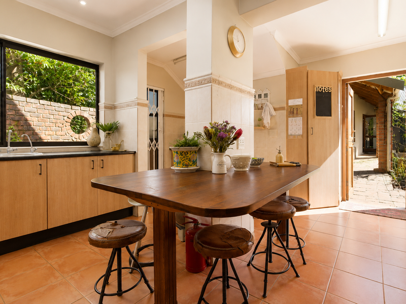 A functional kitchen featuring light wood cabinetry, tiled flooring, and a central dining area with direct access to an outdoor patio space.