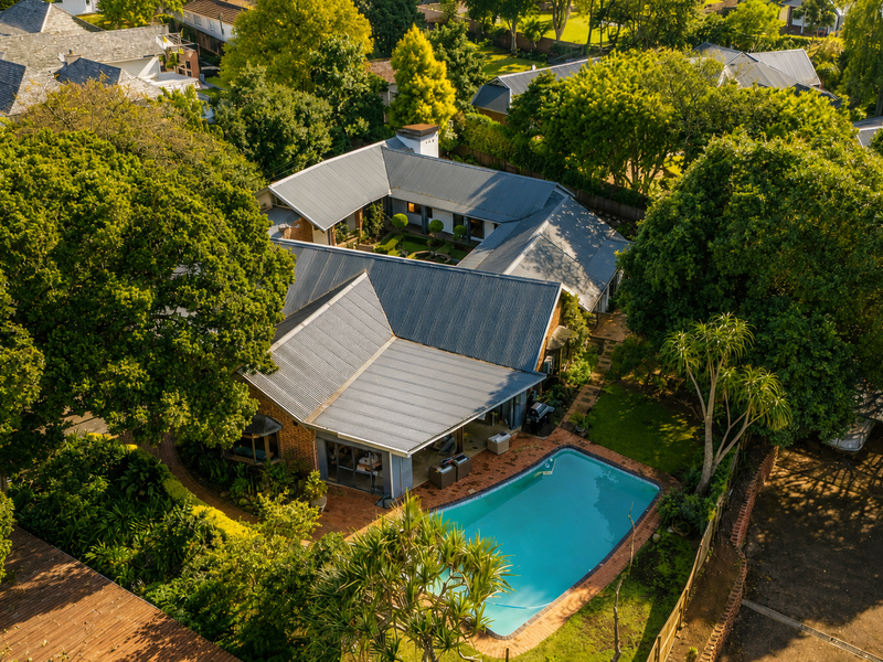 Aerial view of a residential property featuring a swimming pool, landscaped garden, and metal roof structure.